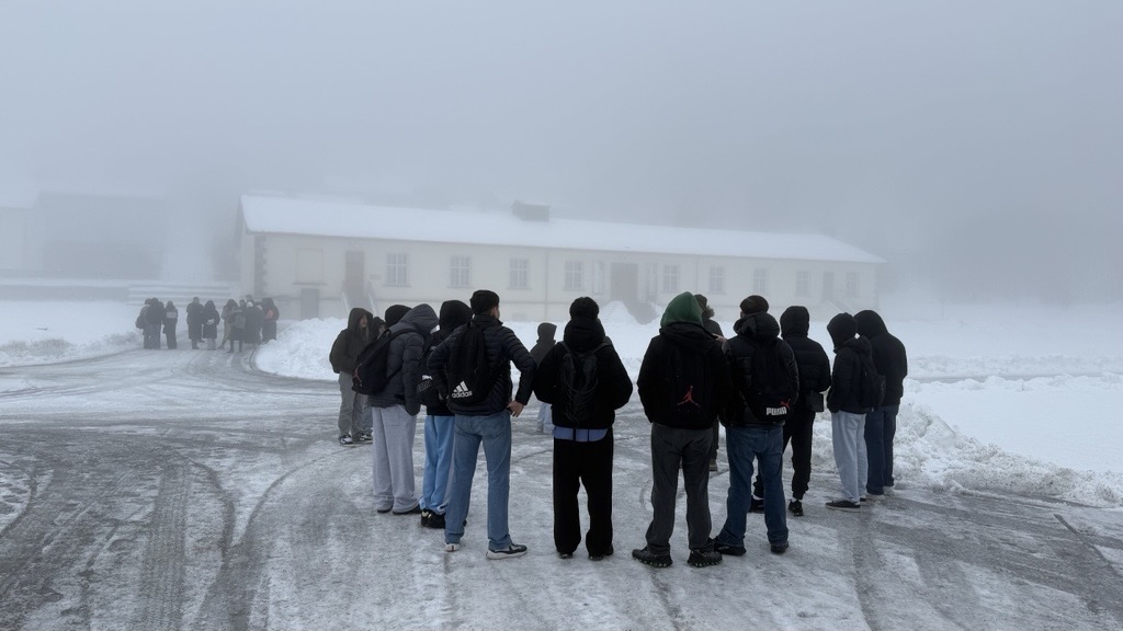 Eine Schülergruppe steht im verschneiten KZ-Gelände und betrachtet ein Gebäude. 