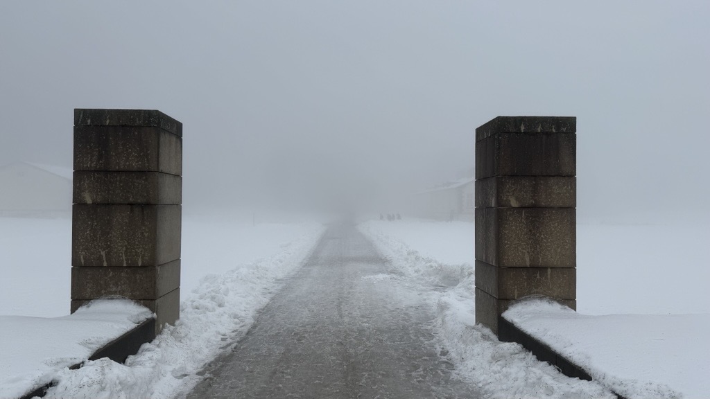 Eine verschneite Landschaft mit langem zentralem Weg, der von zwei gemauerten Eingangssäulen umrahmt wird. 
